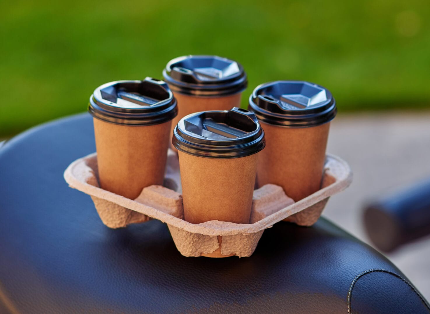 Four paper coffee cups standing on scooter, selective focus. Food delivery concept